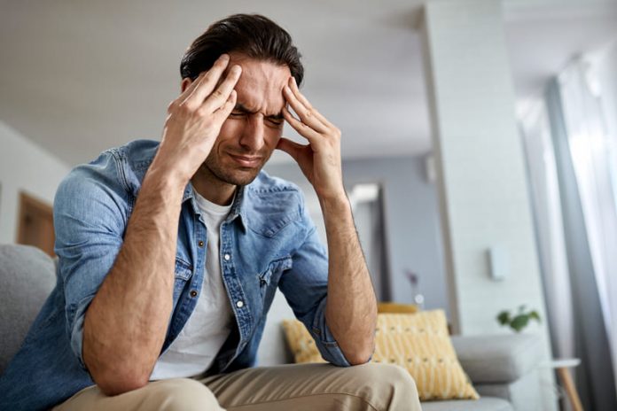 low-angle-view-distraught-man-holding-his-head-pain-while-sitting-living-room (1) migraña
